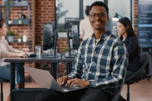 portrait-artificial-intelligence-app-developer-sitting-down-typing-laptop-fixing-glasses-looking-up-smiling-camera-programer-using-portable-computer-innovating-cloud-computing